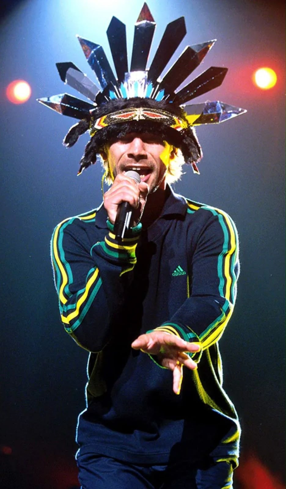Jay Kay de Jamiroquai cantando con un tocado de cristales y una campera Adidas de tres tiras